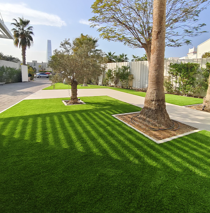 Artificial Grass Dubai Installation In A Large Front Yard Featuring Elegant Paving, Mature Trees, And Vibrant Green Turf.